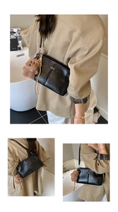 Detail of black glossy leather crossbody bag with metal plaque and cute bear charm