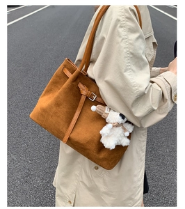 Close-up of brown suede tote bag with leather strap detailing and a white plush toy charm