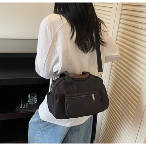 Detailed side view of black multi-pocket nylon shoulder bag with brown leather handles