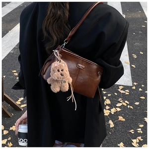 Brown leather shoulder bag with plush dog charm worn by a model in autumn street style