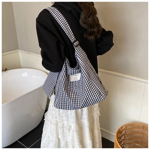 Close-up of checkered canvas tote bag with adjustable shoulder strap on a model
