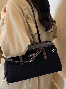 Classic black tote bag with brown trim and shoulder strap worn with a khaki trench coat