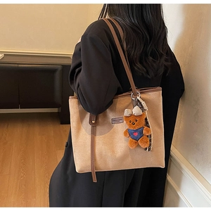 Detail of light brown tote bag featuring a leather logo patch and cute bear keychain