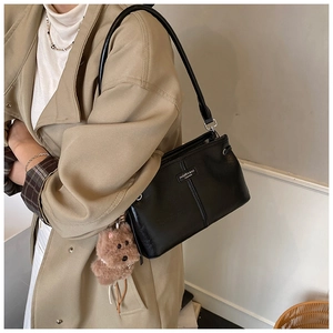 Detailed view of a black leather tote bag with a plush bear charm on a model