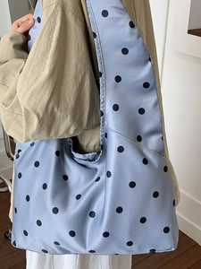 Minimalistische hellblaue Satin-Tragetasche mit schwarzen Punkten an einem weiblichen Model