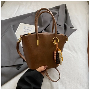 Detail view of dark brown leather bucket bag with wooden bead charm and long shoulder strap