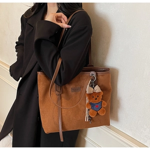 Brown suede tote bag detail with rectangle leather patch and blue heart bear charm