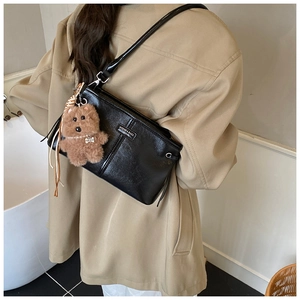 Detail of a black glossy crossbody bag featuring a cute brown teddy bear plush charm