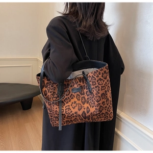 Detail view of large leopard print tote bag featuring black leather handles and logo patch