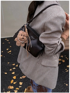 Detail view of black glossy leather bag with a cute plush bear charm and silver logo plate