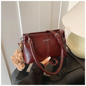 Detail of burgundy leather handbag with fashion logo, zipper, and bear charm accessory
