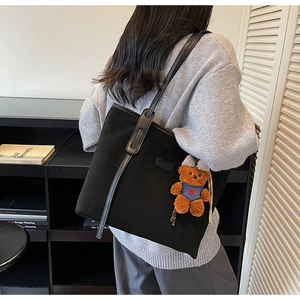 Detail of black tote bag with textured matte finish and cute brown teddy bear charm