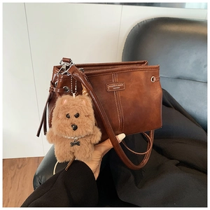 Detail of dark brown leather handbag with vintage stitching and cute plush bear charm