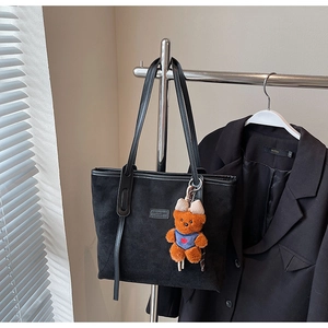 Detail of black suede tote bag with a bear charm and metallic brand nameplate
