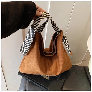 Detail of brown suede tote bag featuring a striped woven shoulder strap and knot decoration