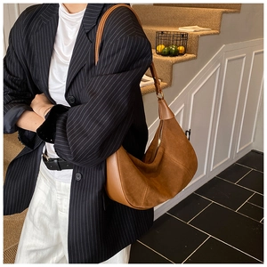 Détail d'un sac demi-lune en daim marron avec passepoil en cuir et fermeture éclair en métal
