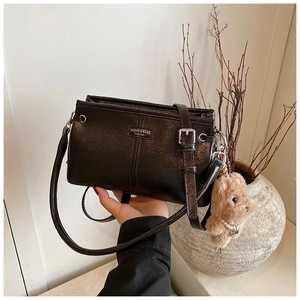 Detail of black leather square bag with metal logo and cute brown bear pendant