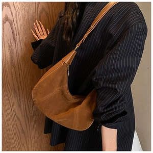 Détail d'un sac demi-lune en daim marron avec coutures verticales et bandoulière