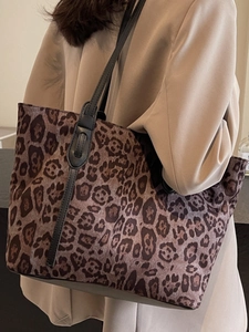 Large leopard print tote bag with black straps worn by a model in a beige suit