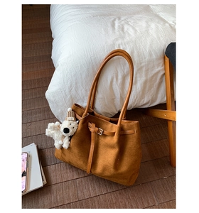 Detail of a large brown suede tote bag with a plush dog charm on a wooden floor
