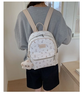Détail d'un sac à dos blanc avec imprimés lapins et pendentif ours en peluche mignon