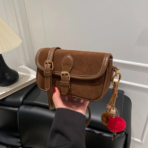 Close-up of brown suede crossbody bag with retro metal buckle and plush pompom charms