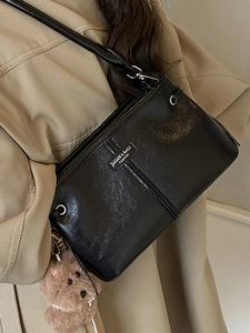 Retro black leather crossbody bag with metal logo and plush bear charm on khaki coat