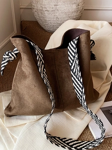 Brown faux suede tote bag with striped woven strap on minimalist chic backdrop