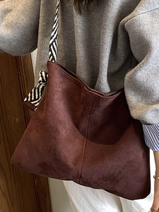 Brown suede tote bag with striped shoulder strap shown in a lifestyle setting