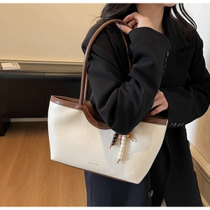 Détail du grand sac cabas crème avec finitions en cuir marron et breloque en perles