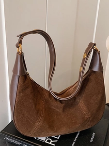 Sac hobo en daim marron avec garniture en cuir et détails dorés sur fond sombre