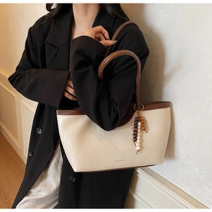 Détail d'un sac cabas crème avec glands en perles de bois et logo de marque