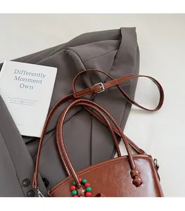 Close-up of brown glossy leather bag with bead charms on grey suit background