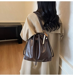 Detail of dark brown leather bucket bag with colorful bead charm on a model's back