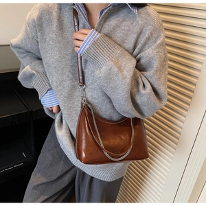 Close-up of brown glossy crescent underarm bag with silver chain and leather strap