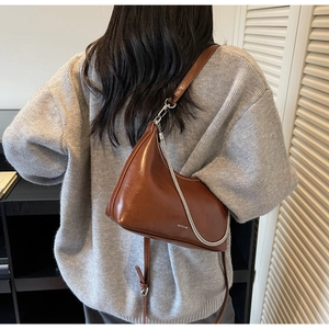 Detail of a brown half-moon bag with high-gloss finish and silver chain decoration