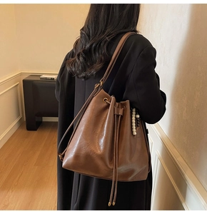 Side view of a vintage brown leather bucket bag with wooden bead charm on a model
