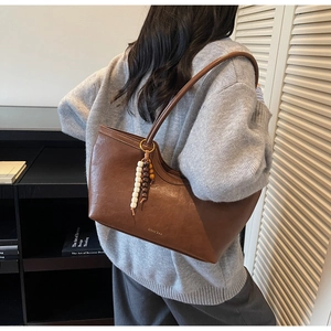 Détail du sac cabas en cuir marron foncé avec pompon en perles colorées porté par un mannequin