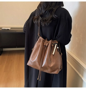 Brown leather bucket bag with drawstring closure and bead tassel detail on model