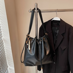 Close-up of black PU leather bucket bag featuring beaded charm and metal eyelets