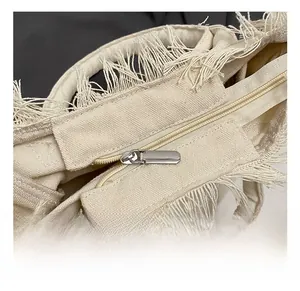 Detailed close-up of silver metal zipper and fringe texture on off-white canvas bag