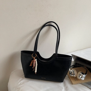 Détail d'un sac cabas en cuir noir avec bord ondulé et breloque décorative en perles