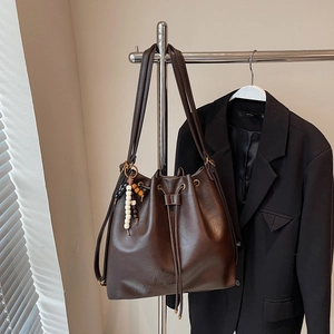 Detail of a dark brown leather bucket bag with drawstring closure and beaded charm decoration