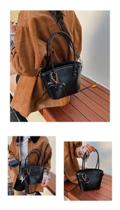 Detail of glossy black leather tote bag with elegant bow and beaded charm on bench
