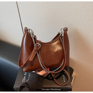 Detailed view of brown glossy underarm bag with silver chain on black books