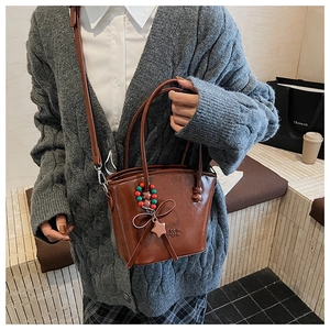 Brown faux leather mini bucket bag with decorative charm shown in a lifestyle setting