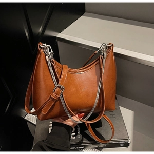 Detail of tan crescent shoulder bag with silver chain and leather strap on dark stairs