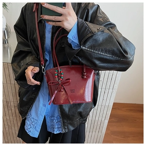 Close-up of a burgundy leather handbag featuring a red bow charm and embossed logo detail