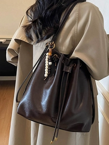 Retro dark brown bucket bag with drawstring closure and bead charm on khaki coat