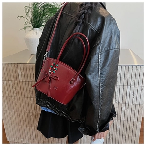 Detail of dark red glossy shoulder bag with bow and star charm on black jacket outfit